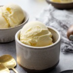 Scoops of olive oil ice cream in ceramic dishes, with gold spoons and bowl of fleur de sel in the foreground