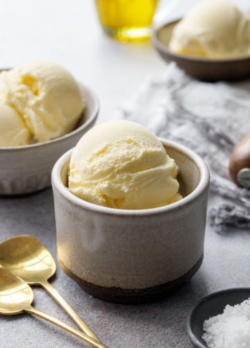 Scoops of olive oil ice cream in ceramic dishes, with gold spoons and bowl of fleur de sel in the foreground