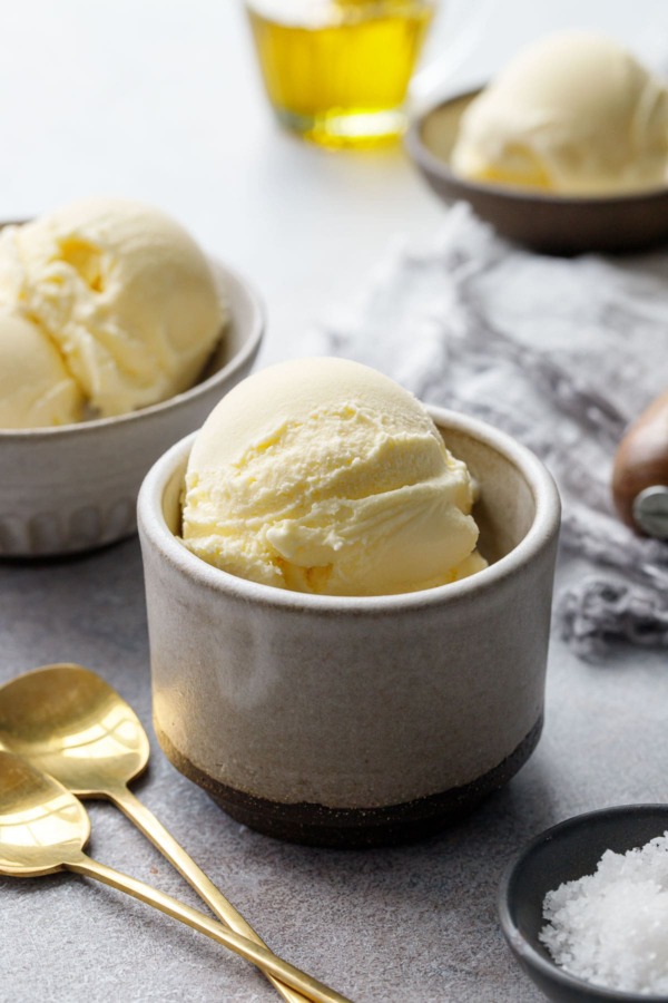 Scoops of olive oil ice cream in ceramic dishes, with gold spoons and bowl of fleur de sel in the foreground