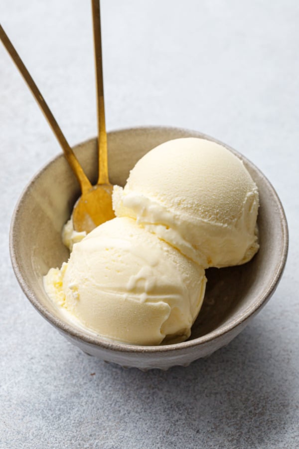 Bowl with two scoops of olive oil ice cream and two brass spoons on gray background