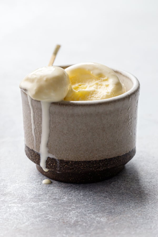 Melty olive oil ice cream with a spoon resting on top of the ceramic cup, drips down the side