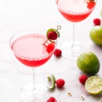 Backlit glasses with bright pink Raspberry Lime Gin Sours, garnished with lime peel and fresh raspberry on a pink marble background.