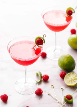 Backlit glasses with bright pink Raspberry Lime Gin Sours, garnished with lime peel and fresh raspberry on a pink marble background.