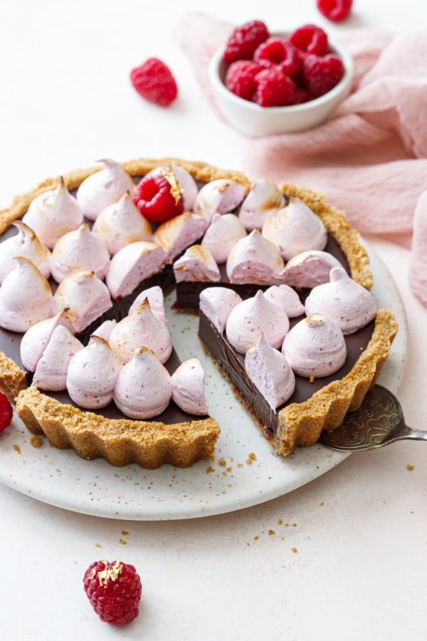 Slices of Chocolate Raspberry S'mores Tart on a light pink cake plate, silver server under one cleanly cut piece.