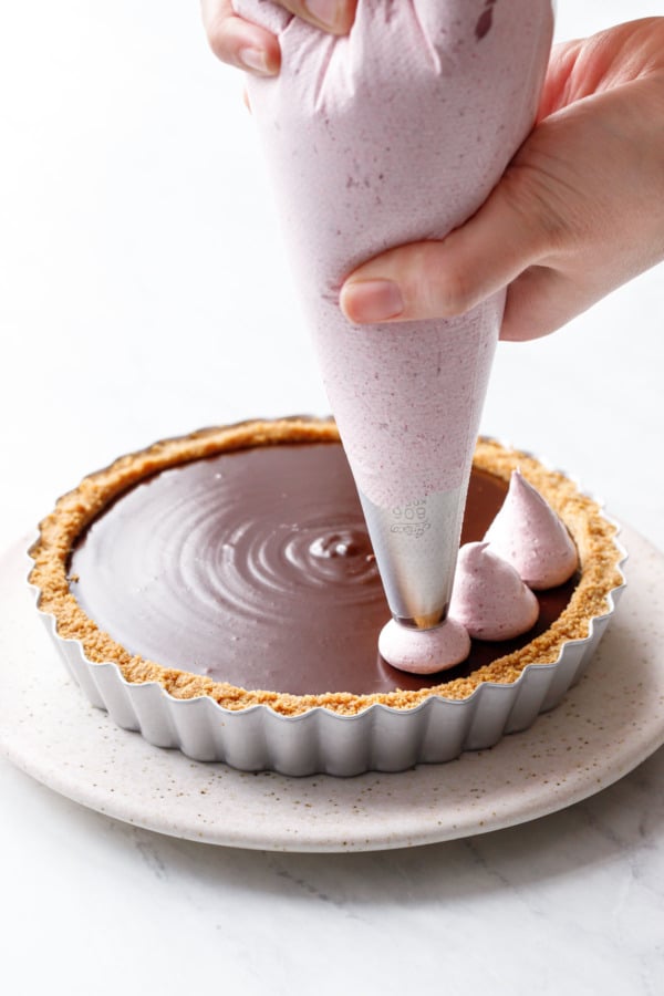 Piping a raspberry marshmallow meringue on top of set chocolate ganache in a graham cracker crust.