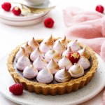 Chocolate Raspberry S'mores Tart on a light pink serving dish, pink linen and fresh raspberries in the background