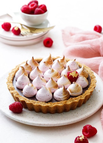 Chocolate Raspberry S'mores Tart on a light pink serving dish, pink linen and fresh raspberries in the background