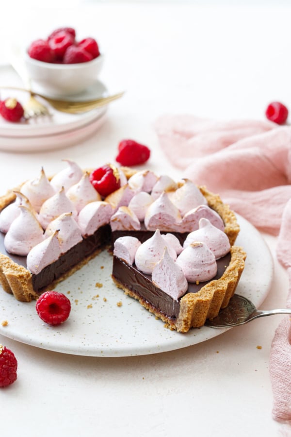 Slices of Chocolate Raspberry S'mores Tart on a light pink cake plate, silver server under one cleanly cut piece.