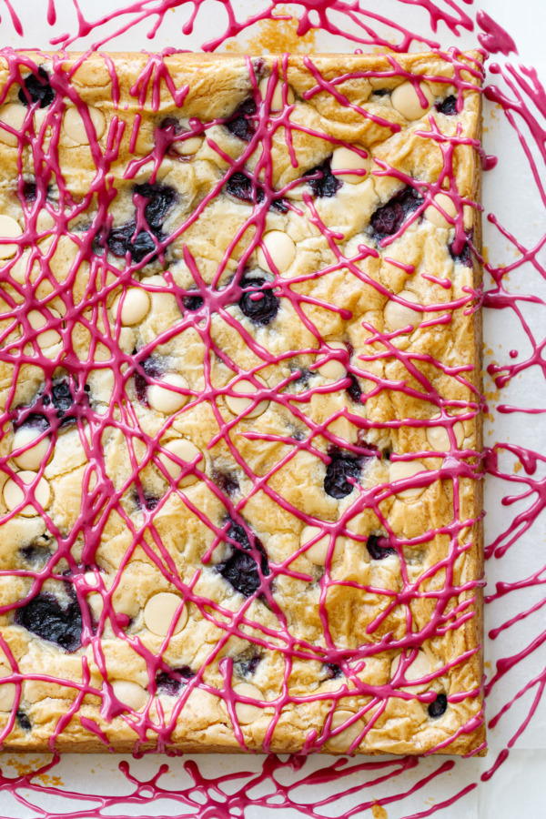 Overhead, artistic drizzles of hot pink blueberry glaze on a square of baked Blueberry White Chocolate Blondies.