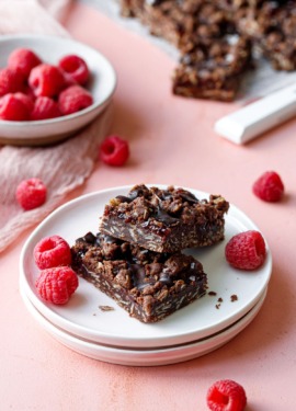 Two Chocolate Raspberry Crumb Bars on a plate with bowl of raspberries and more bars in the background.