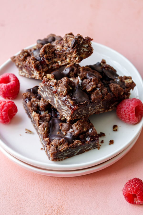 Three Chocolate Raspberry Crumb Bars arranged haphazardly on a plate, with a few fresh raspberries scattered around.