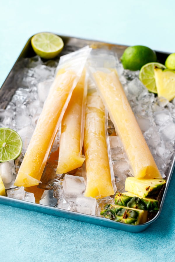 Ice-filled metal tray topped with four frosty Mai Tai Slushy Pops, with crushed ice, limes and pineapple pieces.