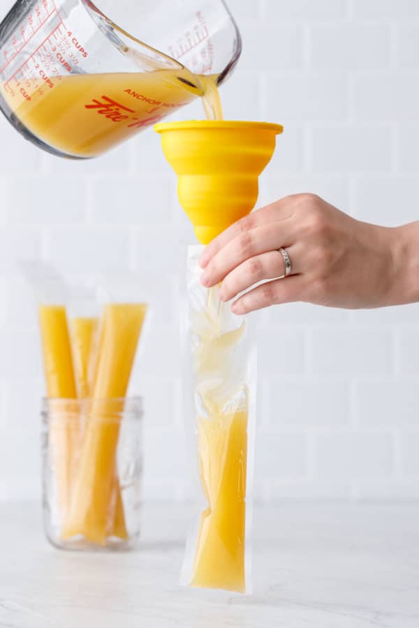 Using a funnel to fill the plastic ice pop sleeves with the Mai Tai base.