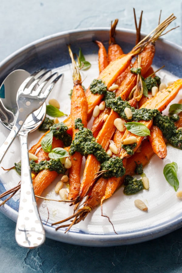 Ceramic platter with pile of Roasted Carrots with Basil and Carrot Top Pesto, silver polka dotted serving utensils.