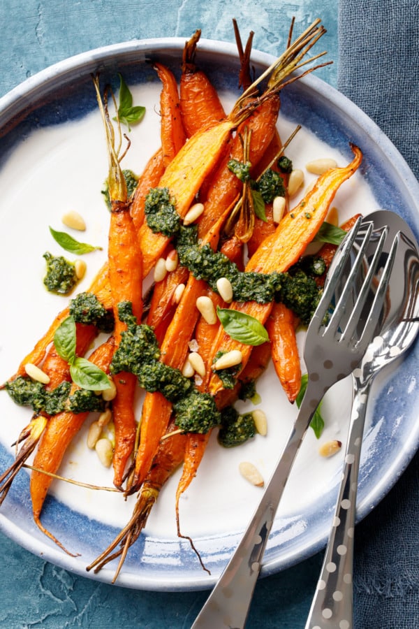 Overhead, round ceramic plate with pile of Roasted Carrots drizzled with Basil and Carrot Top Pesto.