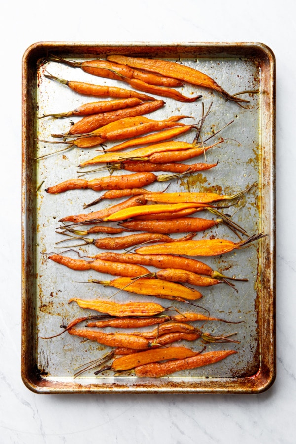 Overhead, silver sheet pan with row of roasted carrots cut in half.