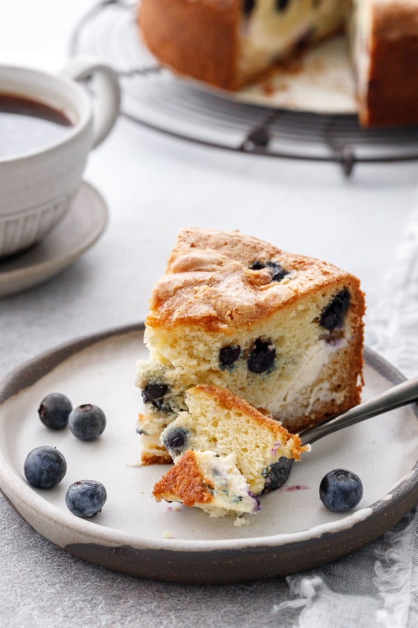 Slice of Blueberry Cream Cheese Coffee Cake on a plate with a bite cut off on a fork on the side.