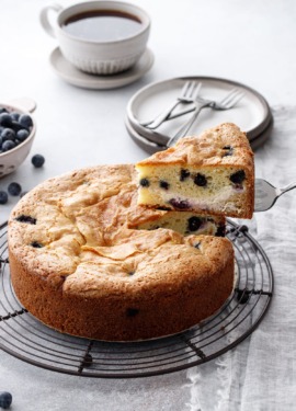 Lifting a cut slice of Blueberry Cream Cheese Coffee Cake on a wire rack, showing the swirl of cream cheese layered inside.