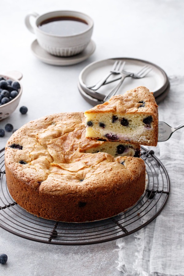 Lifting a cut slice of Blueberry Cream Cheese Coffee Cake on a wire rack, showing the swirl of cream cheese layered inside.