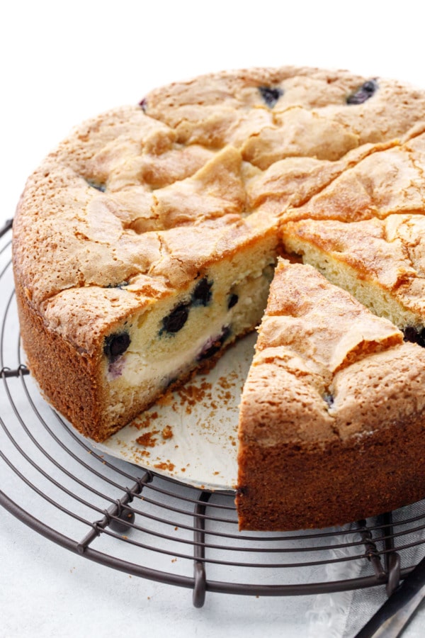 Sliced Blueberry Cream Cheese Coffee Cake on a wire rack, one piece missing to show the interior cross-section.
