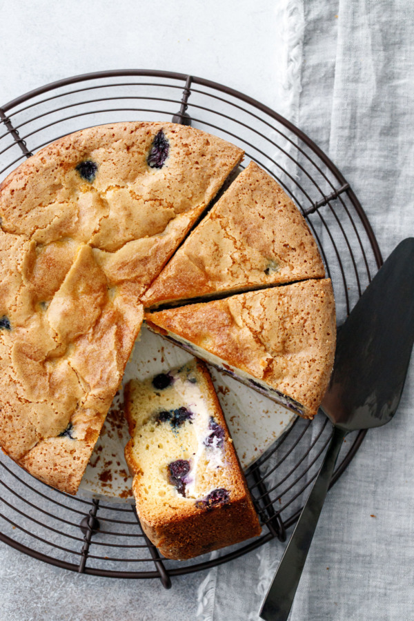 Overhead, sliced round Blueberry Cream Cheese Coffee Cake on a wire rack, one slice on its side to show the interior layers.