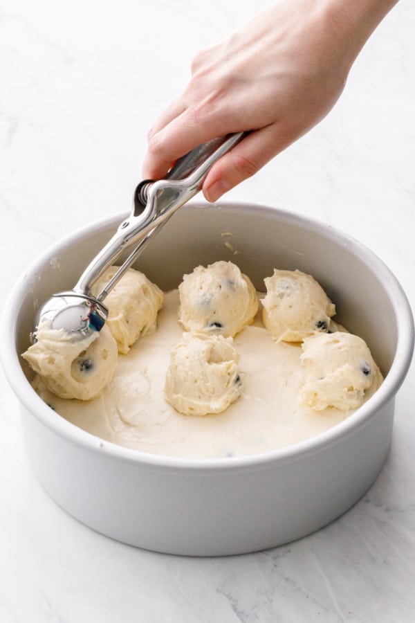 Cookie scoop dropping dollops of batter on top of the cream cheese layer to.