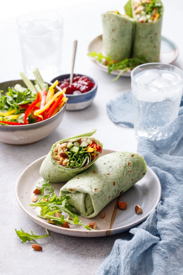 Curried Chicken, Chickpea & Arugula Wraps on plates with blue linen napkin, glasses of water, and bowls of ingredients.