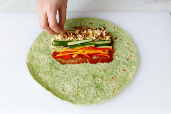 Green spinach wrap laid out on a cutting board with rows of the various ingredients laid out on top.
