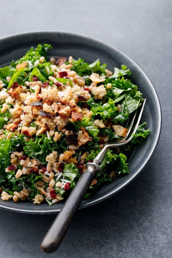 Bowl of Kale & Farro Salad with Sourdough Breadcrumbs with a vintage fork, dark gray background.