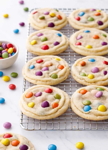 Wire rack with rows of M&M Sugar Cookies, scattered multi-colored M&Ms candies scattered around.