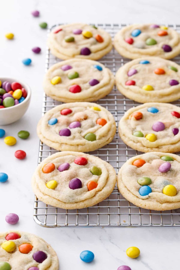 Wire rack with rows of M&M Sugar Cookies, scattered multi-colored M&Ms candies scattered around.