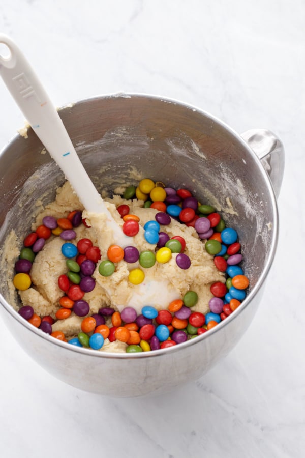 Metal mixing bowl filled with sugar cookie dough and colorful M&Ms candies ready to be mixed in.