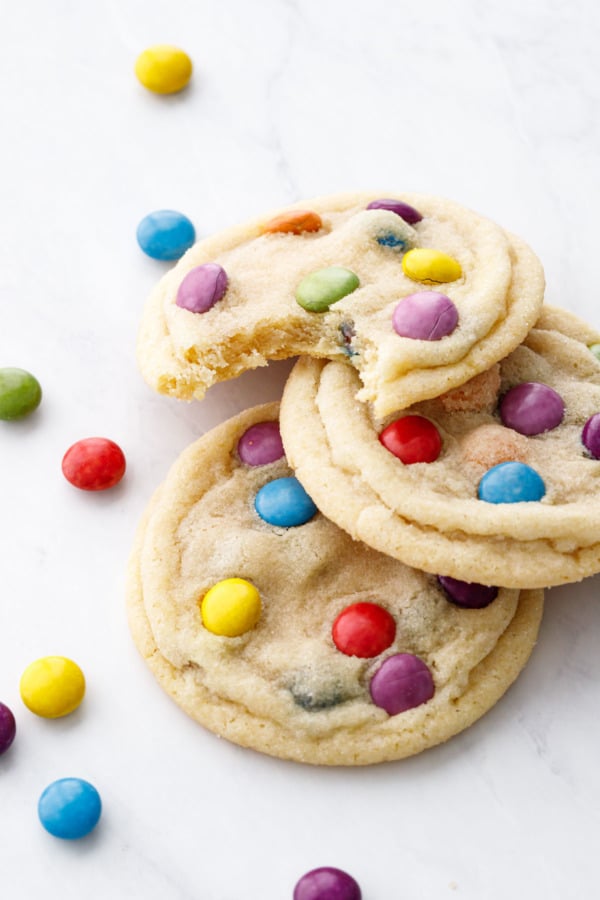 Three M&M Sugar Cookies on a marble background, one cookie with a bite out of it to show texture.