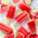 Overhead, Tequila Watermelon Popsicles arranged randomly on crushed ice, with slices of watermelon and lime.