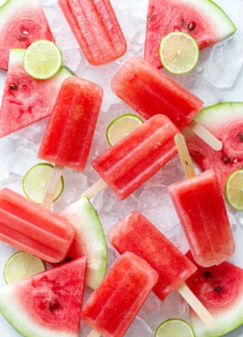 Overhead, Tequila Watermelon Popsicles arranged randomly on crushed ice, with slices of watermelon and lime.