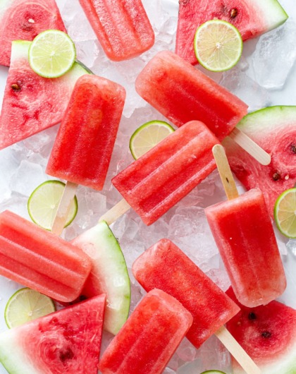 Overhead, Tequila Watermelon Popsicles arranged randomly on crushed ice, with slices of watermelon and lime.