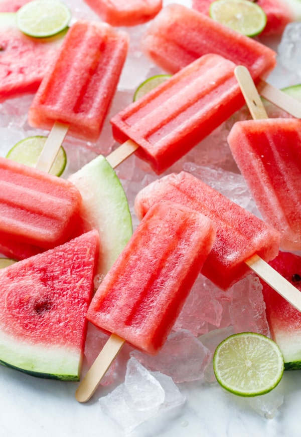 Tequila Watermelon Popsicles, scattered haphazardly on crushed ice with slices of watermelon and lime.