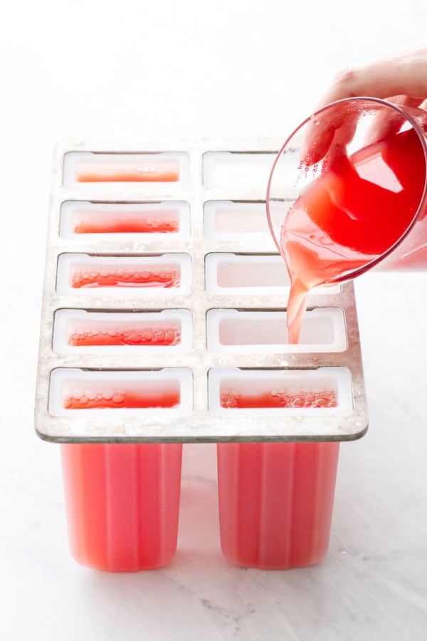 Pouring Tequila Watermelon juice into popsicle molds before freezing.
