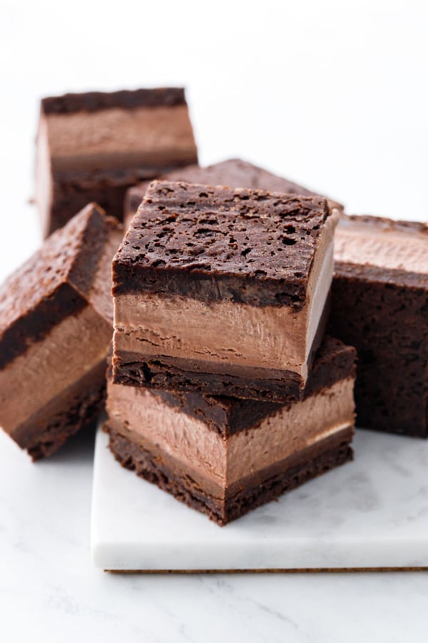 Random stack of Malted Fudge Brownie Ice Cream Sandwiches, cut into squares to show the different layers, on a marble board.