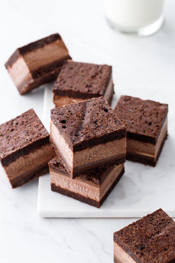 Random stack of Malted Fudge Brownie Ice Cream Sandwiches, cut into squares to show the different layers, on a marble board.