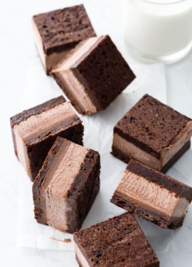 Random arrangement of Malted Fudge Brownie Ice Cream Sandwiches cut into squares, on a crinkled piece of parchment with glass of milk.