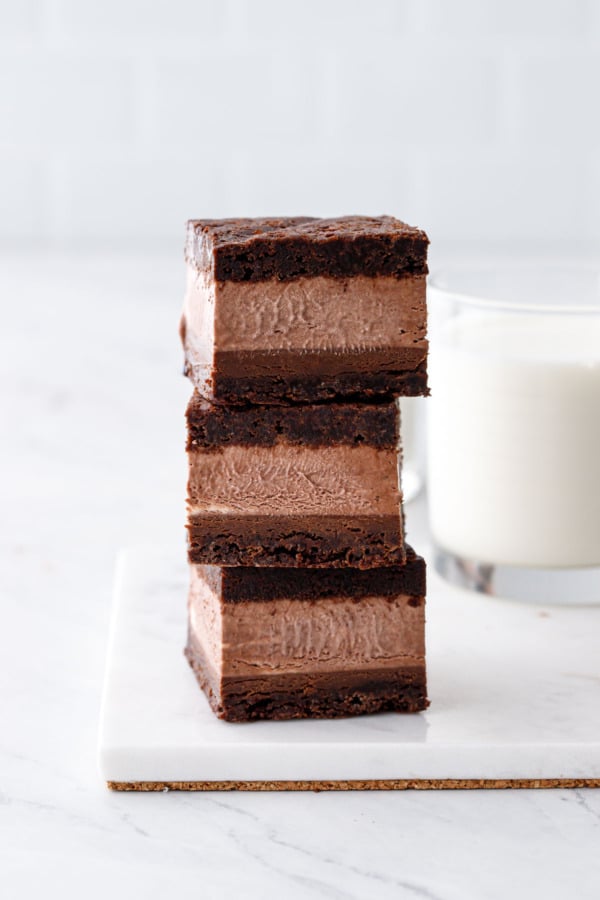 Stack of three Malted Fudge Brownie Ice Cream Sandwiches, on a marble board with glass of milk in the background.