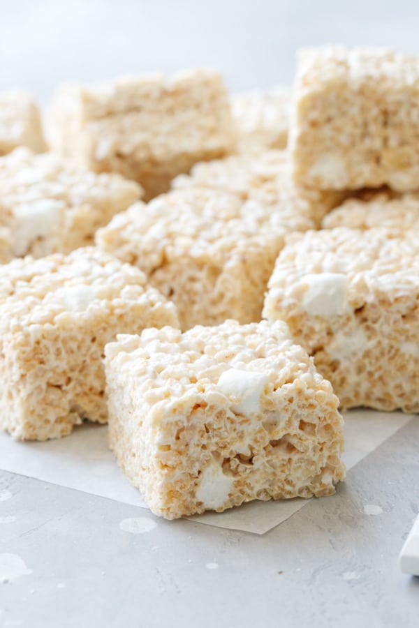 Olive Oil Rice Krispie Treats cut into perfect squares, on a piece of parchment on a gray background.
