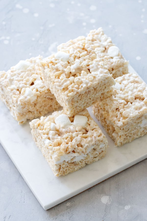 Stack of five square-cut Olive Oil Rice Krispie Treats on a square marble trivet, gray background.