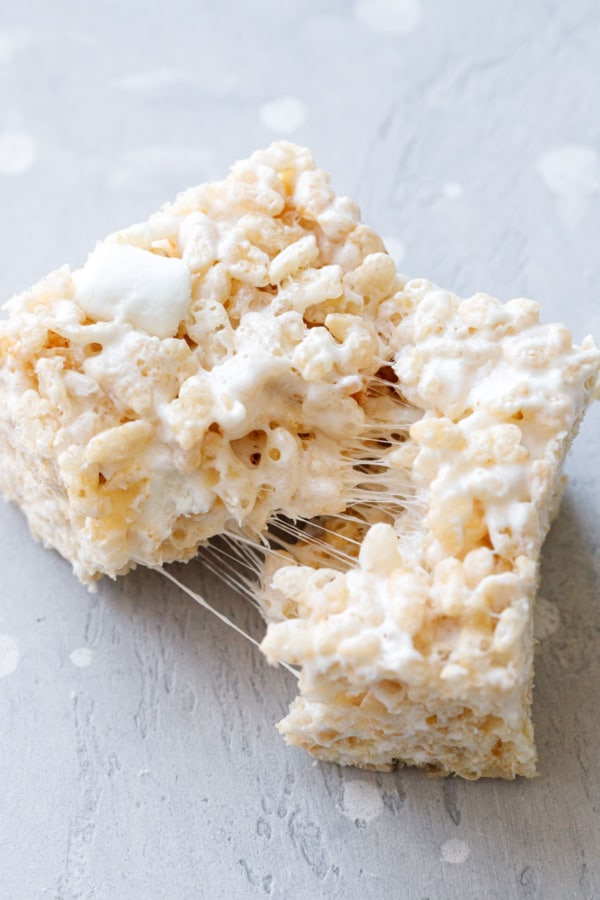 Olive Oil Rice Krispie Treat pulled in half with threads of stretchy marshmallow visible on a gray background.