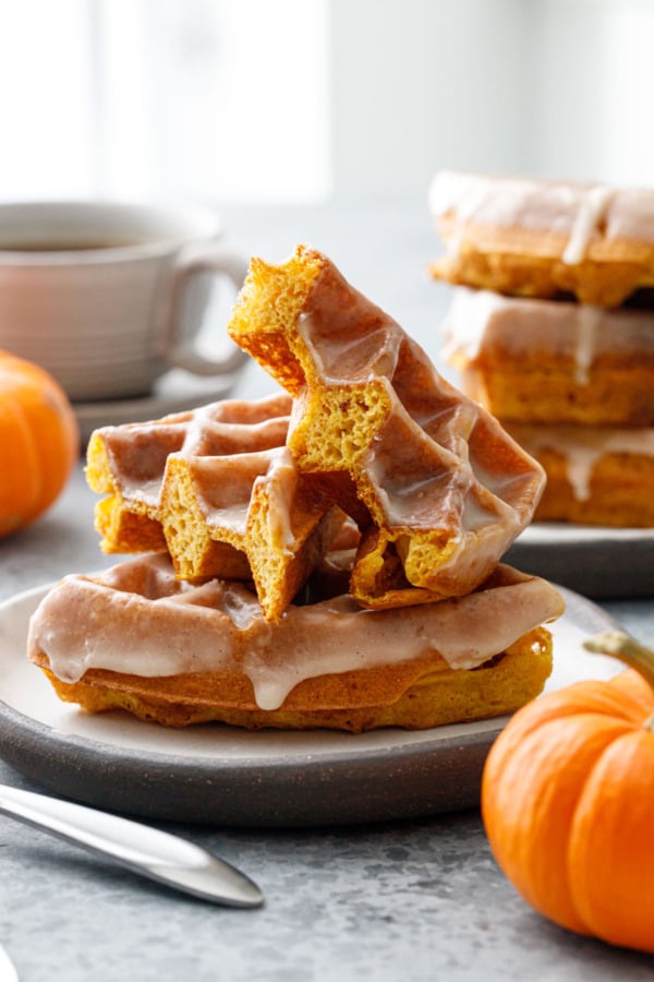 Low angle, two plates with stacks of Glazed Pumpkin Donut Waffles, one waffle cut in half to show the light and airy texture.