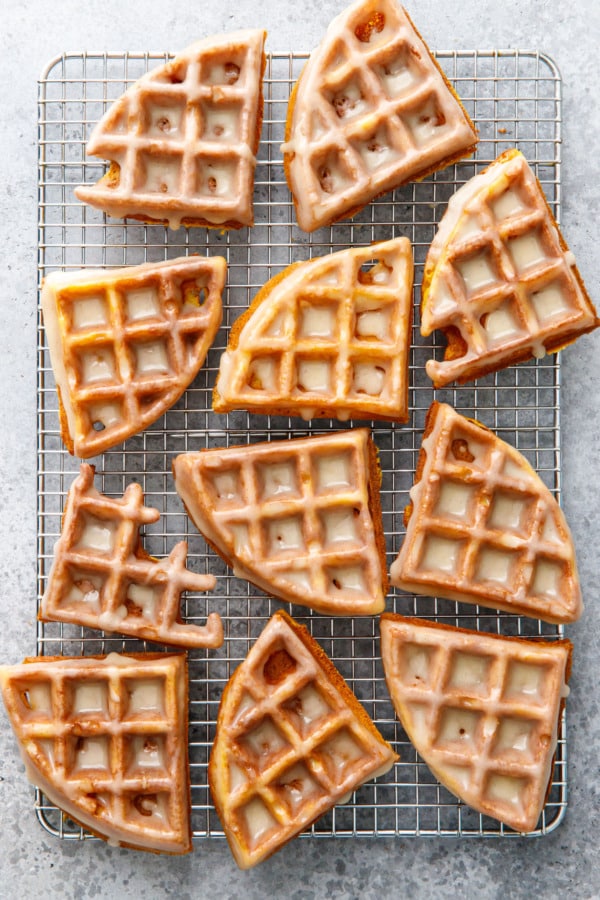 Overhead, wire rack with quarter pieces of Glazed pumpkin donut waffles arranged randomly.