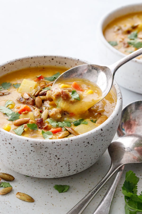 Closeup, spoon lifting a bite of Sausage & Corn Chowder out of a bowl, showing the thick, chunky and creamy texture of the soup.