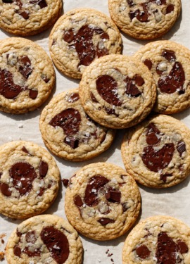 Overhead, baking sheet with randomly arranged Amaretto Chocolate Chip Cookies, with visible flakes of sea salt and melted chocolate puddles.