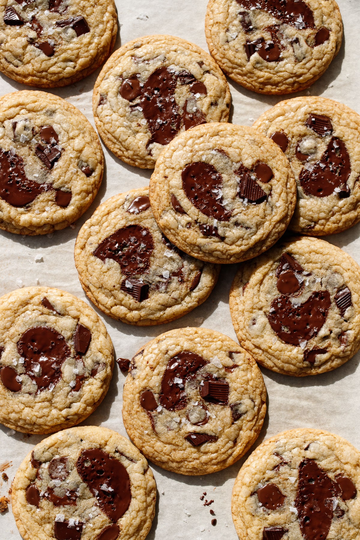 Overhead, baking sheet with randomly arranged Amaretto Chocolate Chip Cookies, with visible flakes of sea salt and melted chocolate puddles.